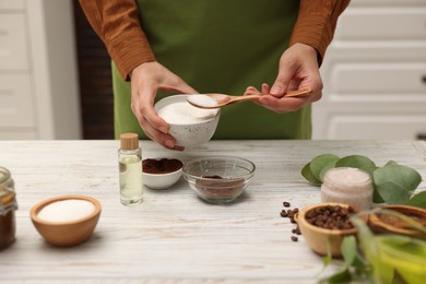 Photo of Making natural scrub. Woman adding sugar into bowl at white wooden table, closeup