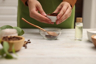 Photo of Making natural scrub. Woman adding coffee into bowl at white wooden table, closeup