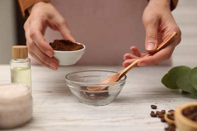 Photo of Making natural scrub. Woman adding coffee into bowl at white wooden table, closeup