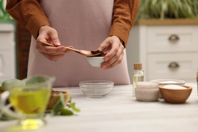 Photo of Making natural scrub. Woman adding coffee into bowl at white wooden table, closeup
