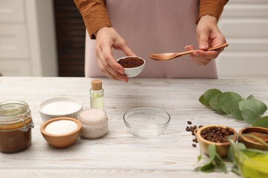 Photo of Making natural scrub. Woman adding coffee into bowl at white wooden table, closeup