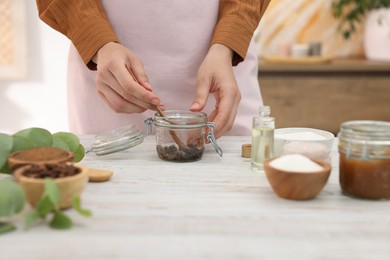 Photo of Woman making natural body scrub at white wooden table, closeup