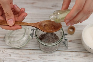 Photo of Making natural scrub. Woman adding essential oil into jar at white wooden table, closeup
