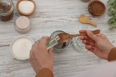 Photo of Making natural scrub. Woman adding essential oil into jar at white wooden table, above view