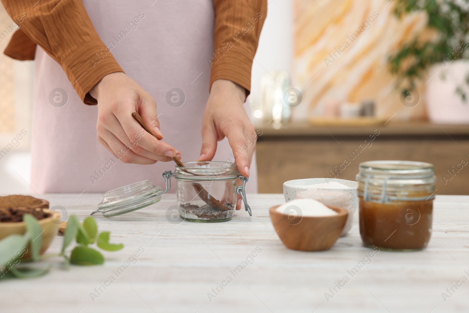 Photo of Woman making natural body scrub at white wooden table, closeup