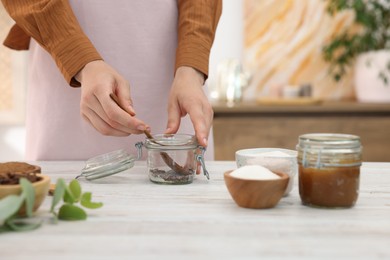 Photo of Woman making natural body scrub at white wooden table, closeup
