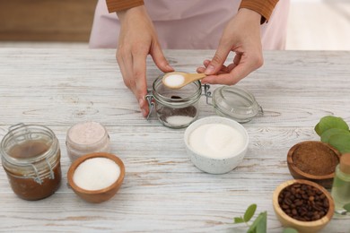 Photo of Making natural scrub. Woman adding sugar into jar at white wooden table, closeup
