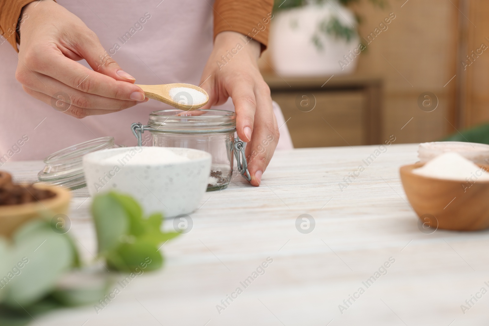 Photo of Making natural scrub. Woman adding sugar into jar at white wooden table, closeup
