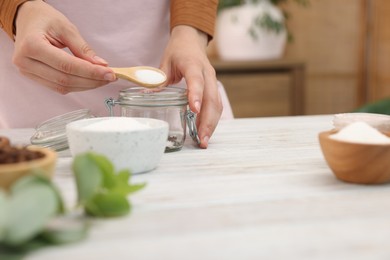 Photo of Making natural scrub. Woman adding sugar into jar at white wooden table, closeup