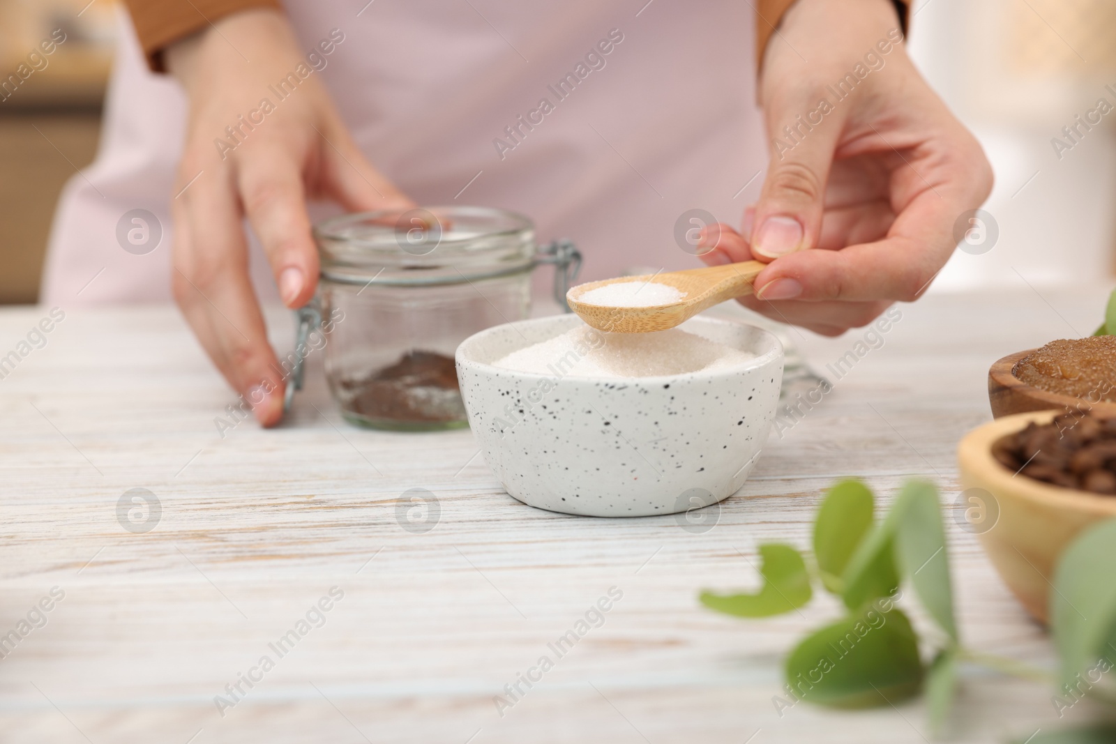 Photo of Making natural scrub. Woman adding sugar into jar at white wooden table, closeup