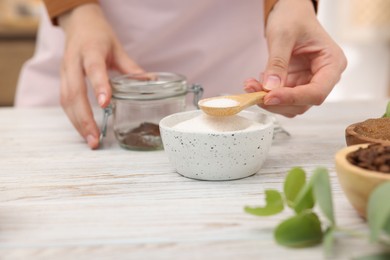 Photo of Making natural scrub. Woman adding sugar into jar at white wooden table, closeup