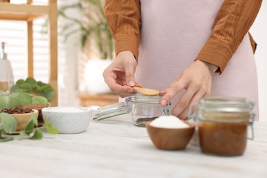 Photo of Woman making natural body scrub at white wooden table, closeup
