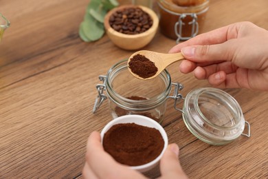 Photo of Making natural scrub. Woman adding coffee into jar at wooden table, closeup