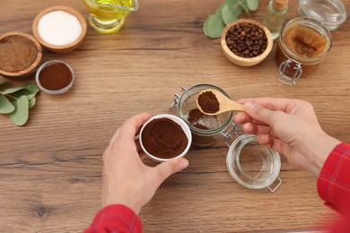 Photo of Making natural scrub. Woman adding coffee into jar at wooden table, top view