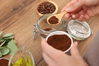 Photo of Making natural scrub. Woman adding coffee into jar at wooden table, closeup