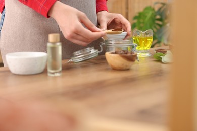 Photo of Making natural scrub. Woman adding coffee into jar at wooden table, closeup