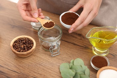 Photo of Making natural scrub. Woman adding coffee into jar at wooden table, closeup