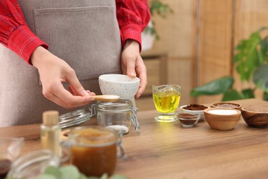 Photo of Making natural scrub. Woman adding sugar into jar at wooden table, closeup