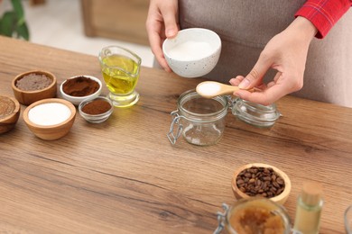 Photo of Making natural scrub. Woman adding sugar into jar at wooden table, closeup