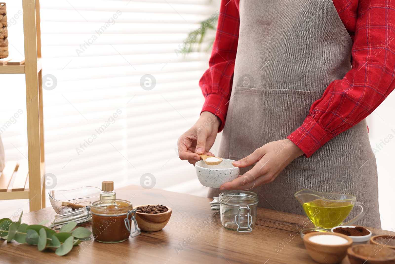 Photo of Making natural scrub. Woman adding sugar into jar at wooden table, closeup