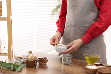 Photo of Making natural scrub. Woman adding sugar into jar at wooden table, closeup