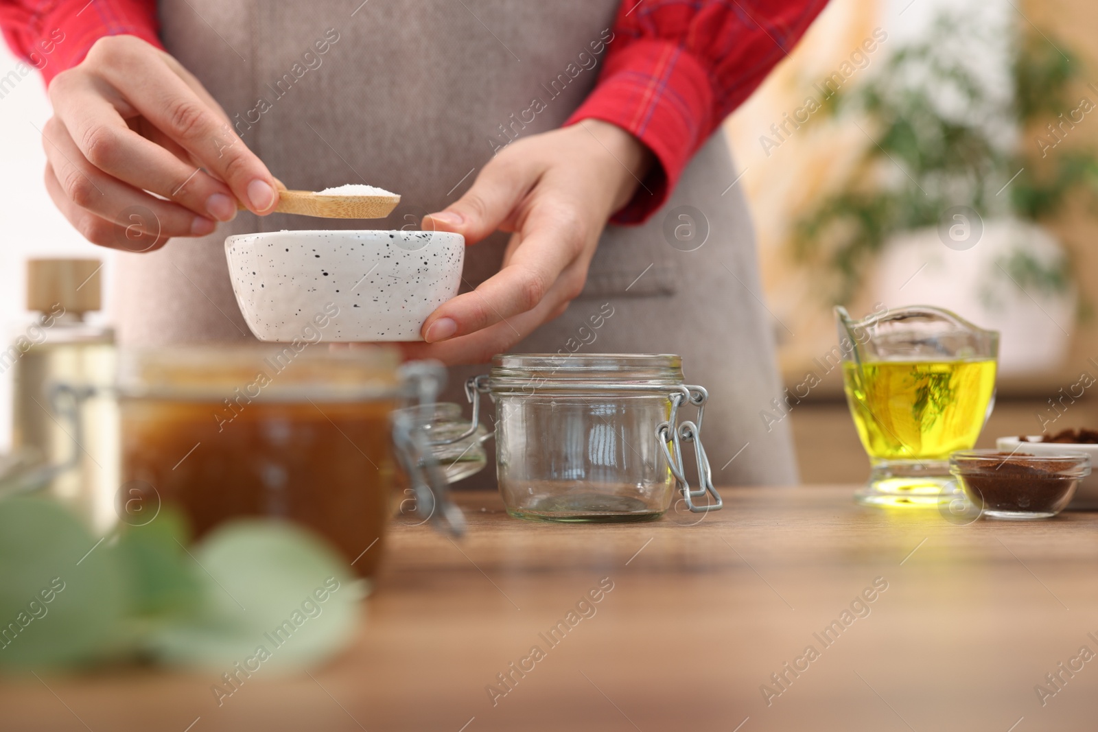Photo of Making natural scrub. Woman adding sugar into jar at wooden table, closeup