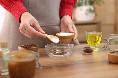 Photo of Making natural scrub. Woman adding sugar into bowl at wooden table, closeup