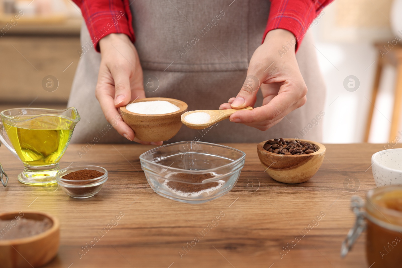 Photo of Making natural scrub. Woman adding sugar into bowl at wooden table, closeup