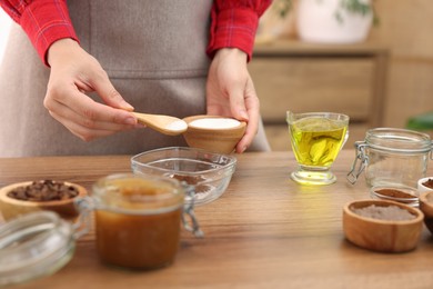 Photo of Making natural scrub. Woman adding sugar into bowl at wooden table, closeup