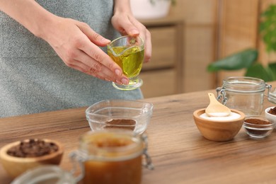 Photo of Making natural scrub. Woman adding oil into bowl at wooden table, closeup