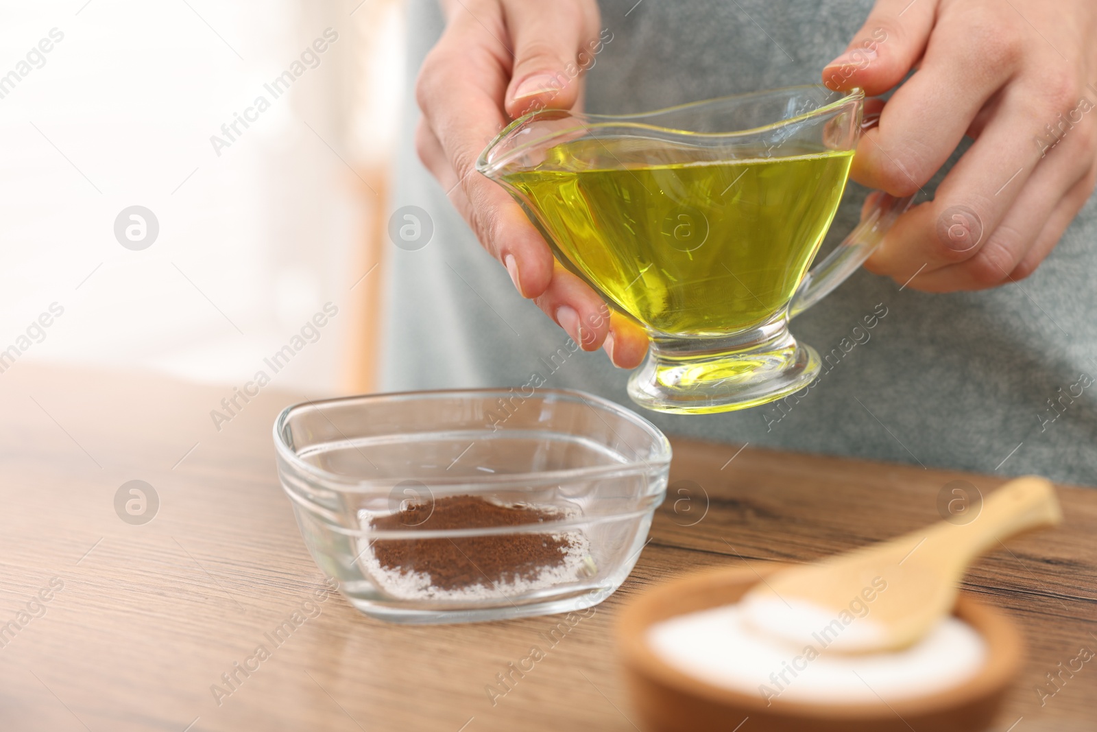 Photo of Making natural scrub. Woman adding oil into bowl at wooden table, closeup