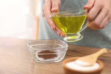 Photo of Making natural scrub. Woman adding oil into bowl at wooden table, closeup