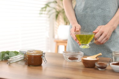 Photo of Making natural scrub. Woman adding oil into bowl at wooden table, closeup