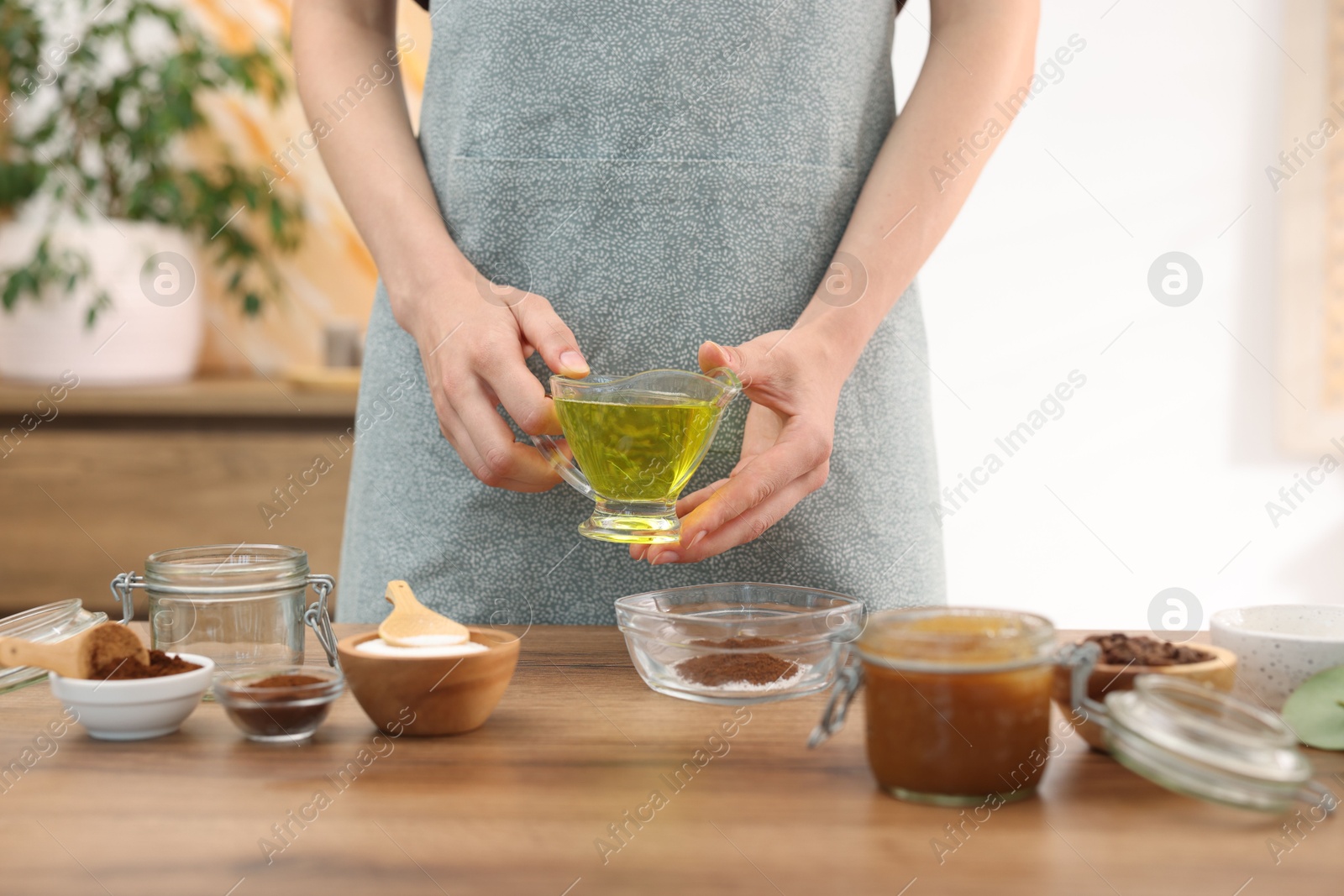 Photo of Making natural scrub. Woman adding oil into bowl at wooden table, closeup