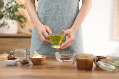 Photo of Making natural scrub. Woman adding oil into bowl at wooden table, closeup