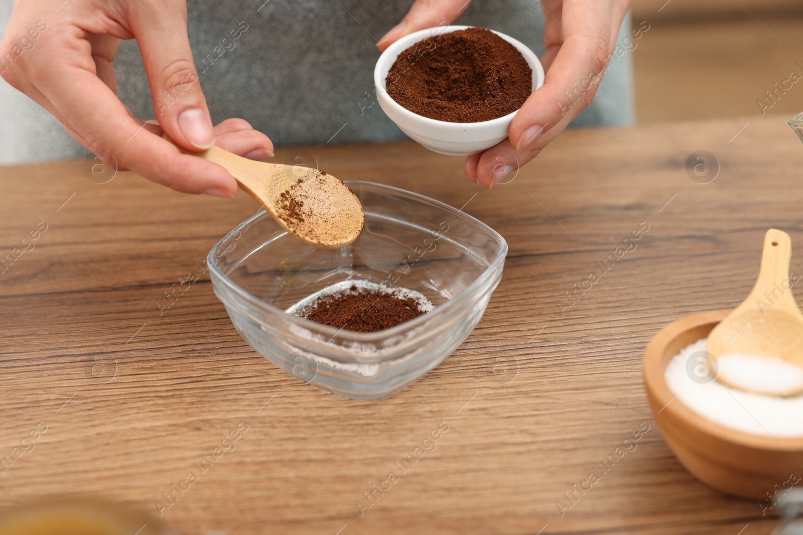Photo of Making natural scrub. Woman adding coffee into bowl at wooden table, closeup