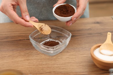 Photo of Making natural scrub. Woman adding coffee into bowl at wooden table, closeup