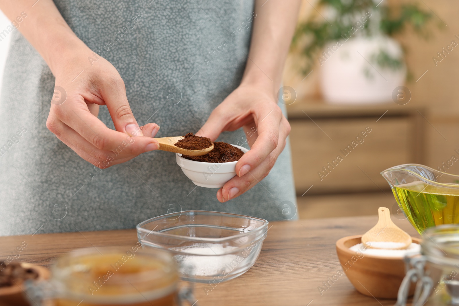Photo of Making natural scrub. Woman adding coffee into bowl at wooden table, closeup