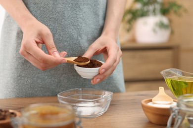 Photo of Making natural scrub. Woman adding coffee into bowl at wooden table, closeup