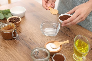 Photo of Making natural scrub. Woman adding coffee into bowl at wooden table, closeup