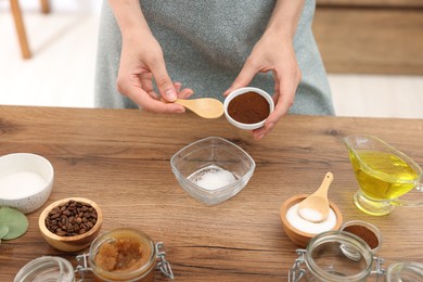 Photo of Making natural scrub. Woman adding coffee into bowl at wooden table, closeup