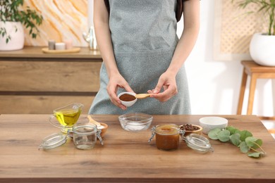 Photo of Making natural scrub. Woman adding coffee into bowl at wooden table, closeup