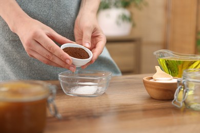 Photo of Making natural scrub. Woman adding coffee into bowl at wooden table, closeup