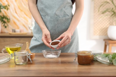 Photo of Making natural scrub. Woman adding coffee into bowl at wooden table, closeup