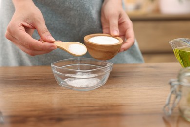 Photo of Making natural scrub. Woman adding sugar into bowl at wooden table, closeup
