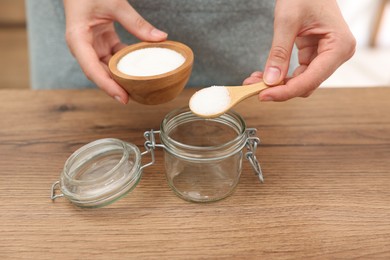 Photo of Making natural scrub. Woman adding sugar into jar at wooden table, closeup