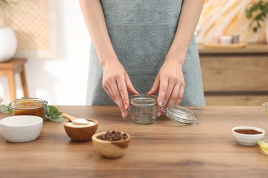 Photo of Woman making natural body scrub at wooden table, closeup
