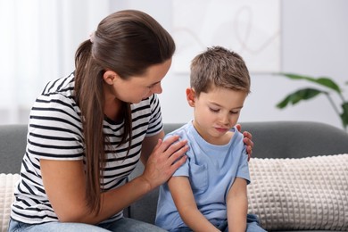 Photo of Mother supporting her sad son on sofa at home