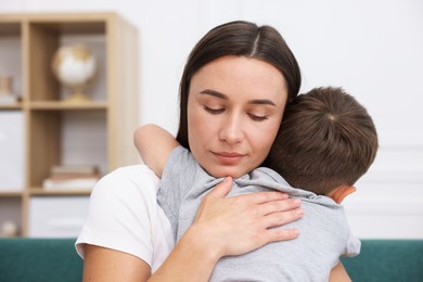 Photo of Mother supporting and hugging her sad son on sofa at home