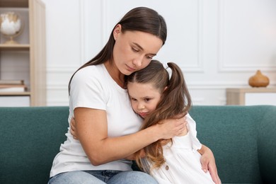 Photo of Mother supporting and hugging her sad daughter on sofa at home